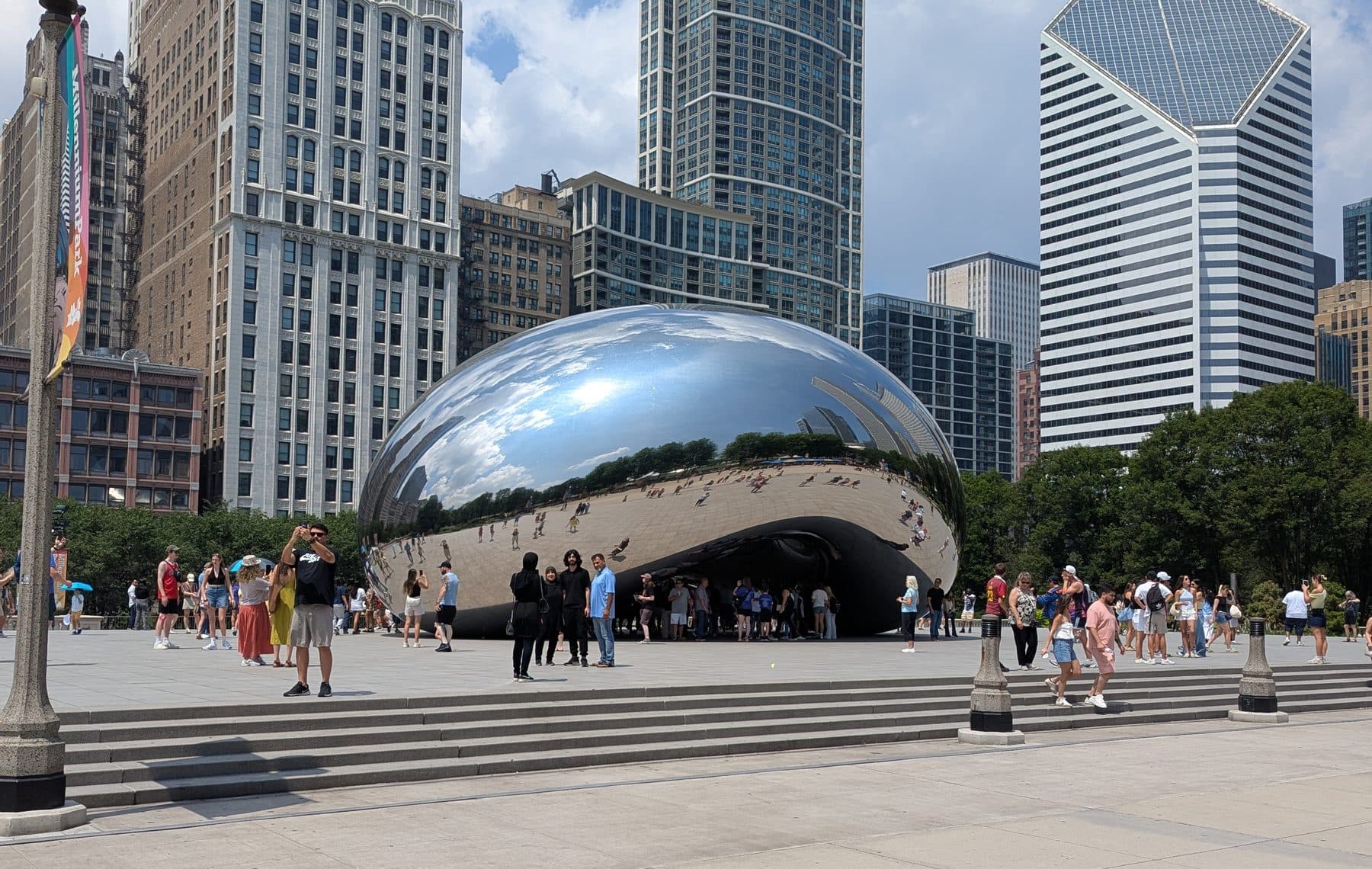 Cloud Gate in Millennium Park at midday, with the Crain Communications Building behind it.