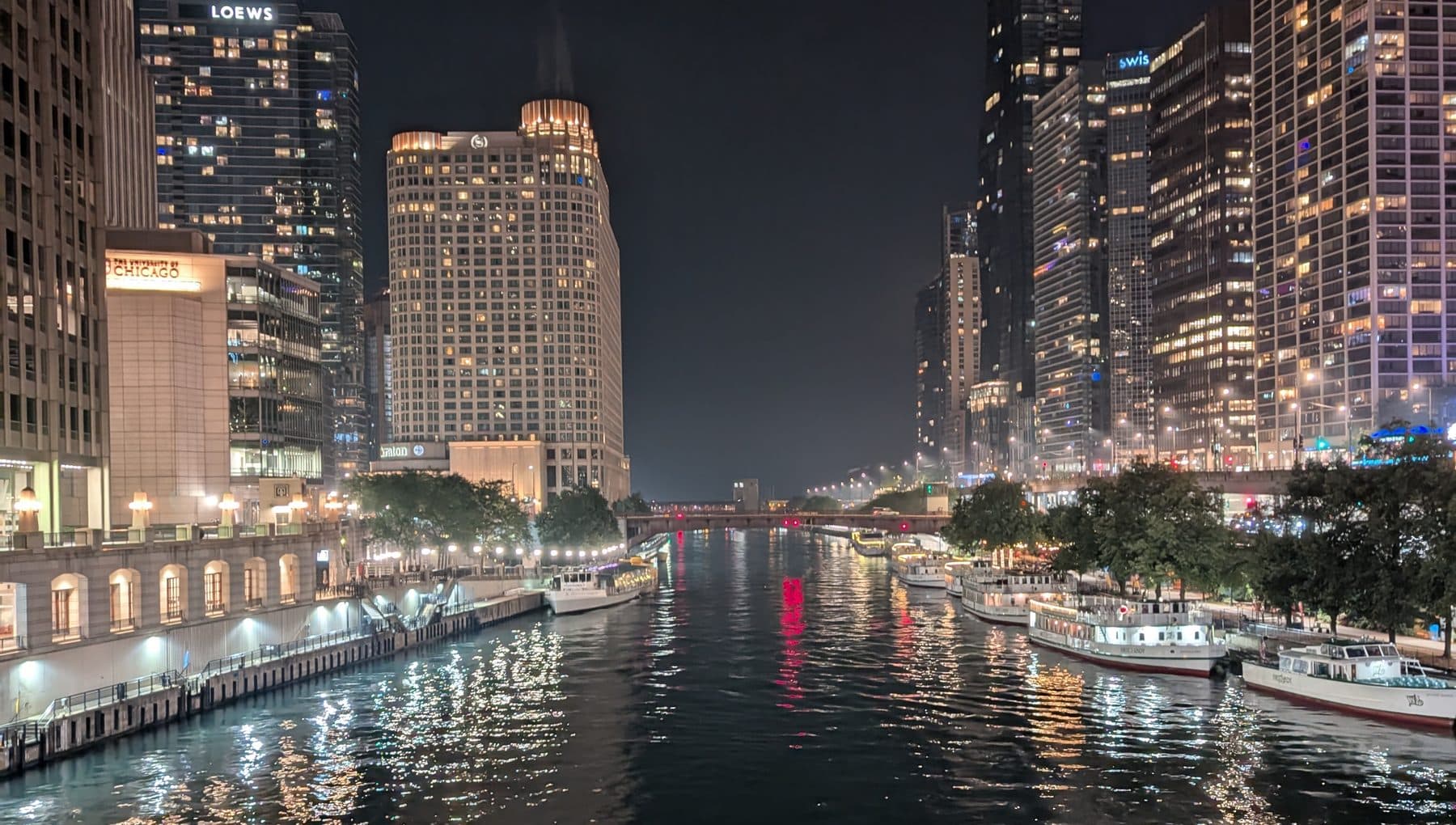 The Chicago River at night with tour boats moored along both banks and the riverwalk lit up.